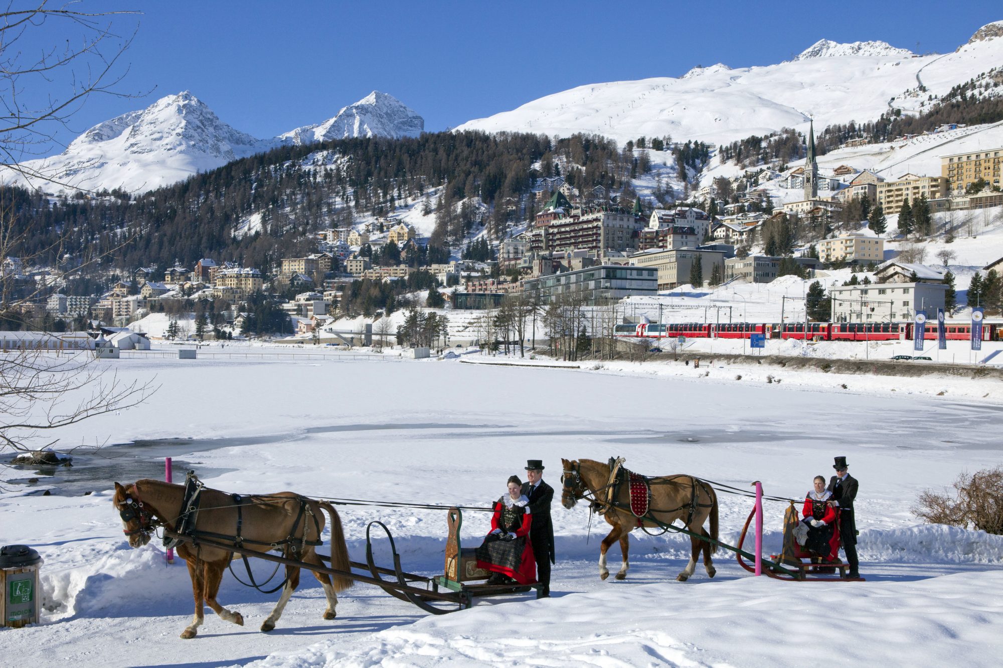 ENGADIN ST. MORITZ - The Schlitteda, an Engadin folk custom, by Lake St. Moritz. The women are dressed in Engadin Sunday costume. View of frozen Lake St. Moritz and of St. Moritz Dorf with Badrutt's Palace Hotel. In background the Piz Albana (3082m), Piz Gueglia (3192m) and the Corviglia ski area with the Piz Nair (3022m). Copyright by: ENGADIN St. Moritz By-line: swiss-image.ch/Christof Sonderegger