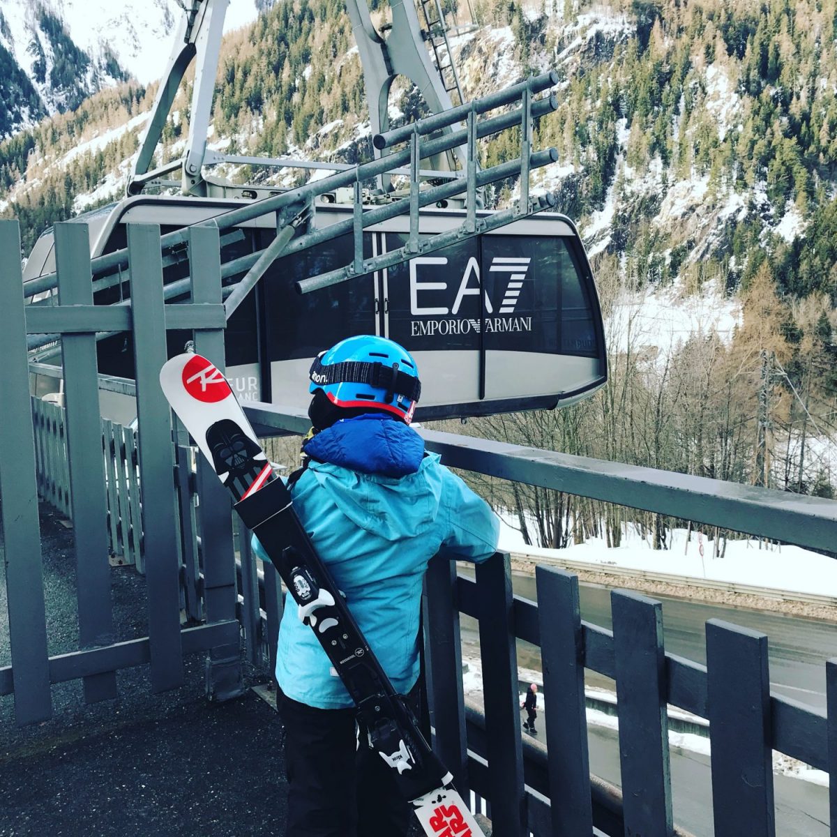 My youngest carrying his own skis with his ski strap waiting the Armani funicular to go to Plan Chécrouit in Courmayeur Mont Blanc. 7 things that can help you when taking kids skiing.