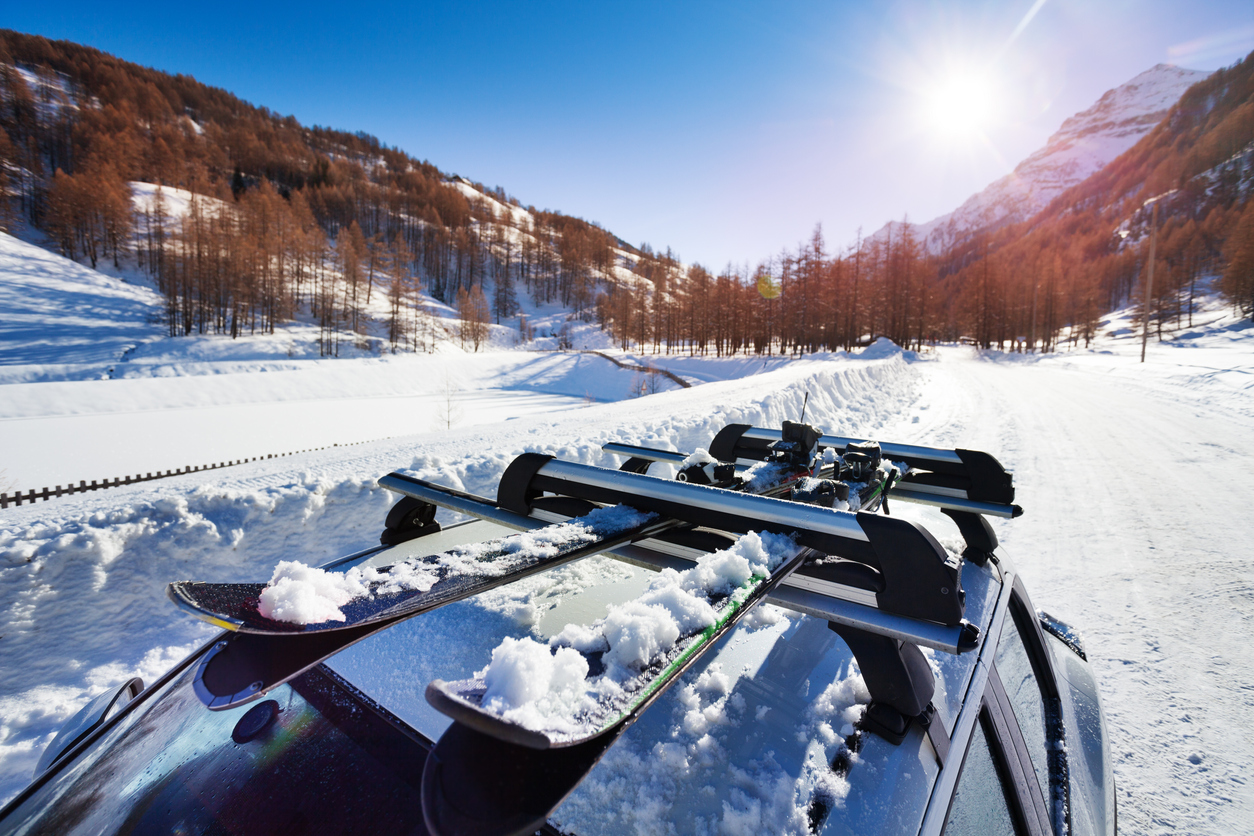 Beautiful view of sunny snowcapped mountains with skis fastened on car roof rails in the foreground. Photo: ICarhireinsurance.com. Skiers Over New Year Prepare for a £450 Wipeout at the Car Hire Rental Desk.